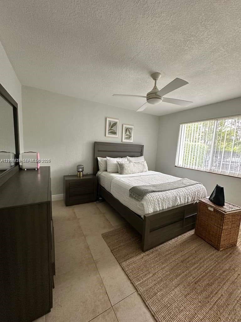 Neutral-toned interior space featuring oversized tile flooring, a white ceiling fan, and large windows with vertical blinds