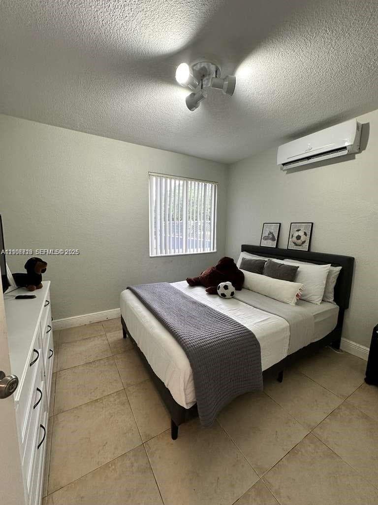 Interior space featuring large-format tile flooring, a wall-mounted ductless air conditioning unit, vertical window blinds, and a multi-directional track light fixture