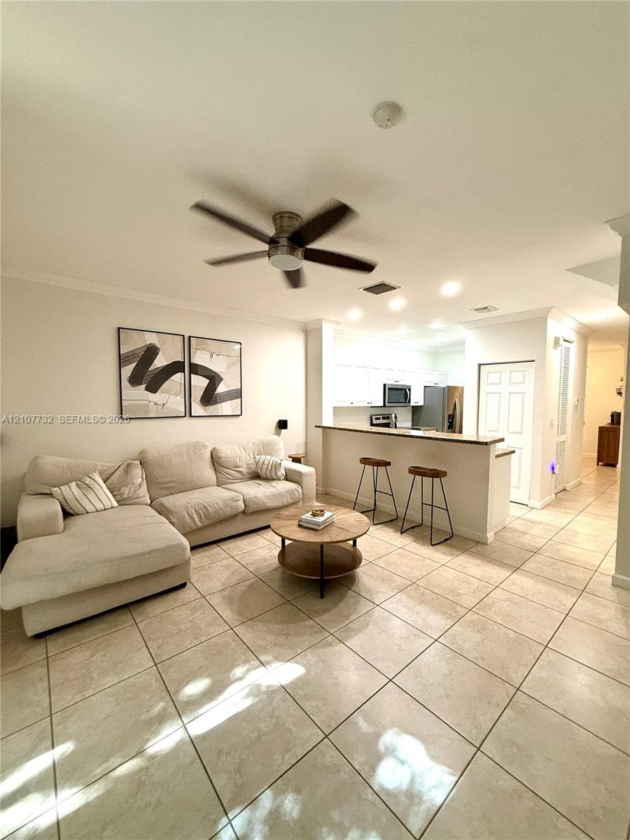 Large-format tile flooring, recessed lighting, multi-blade ceiling fan, and a breakfast bar with a solid-surface countertop