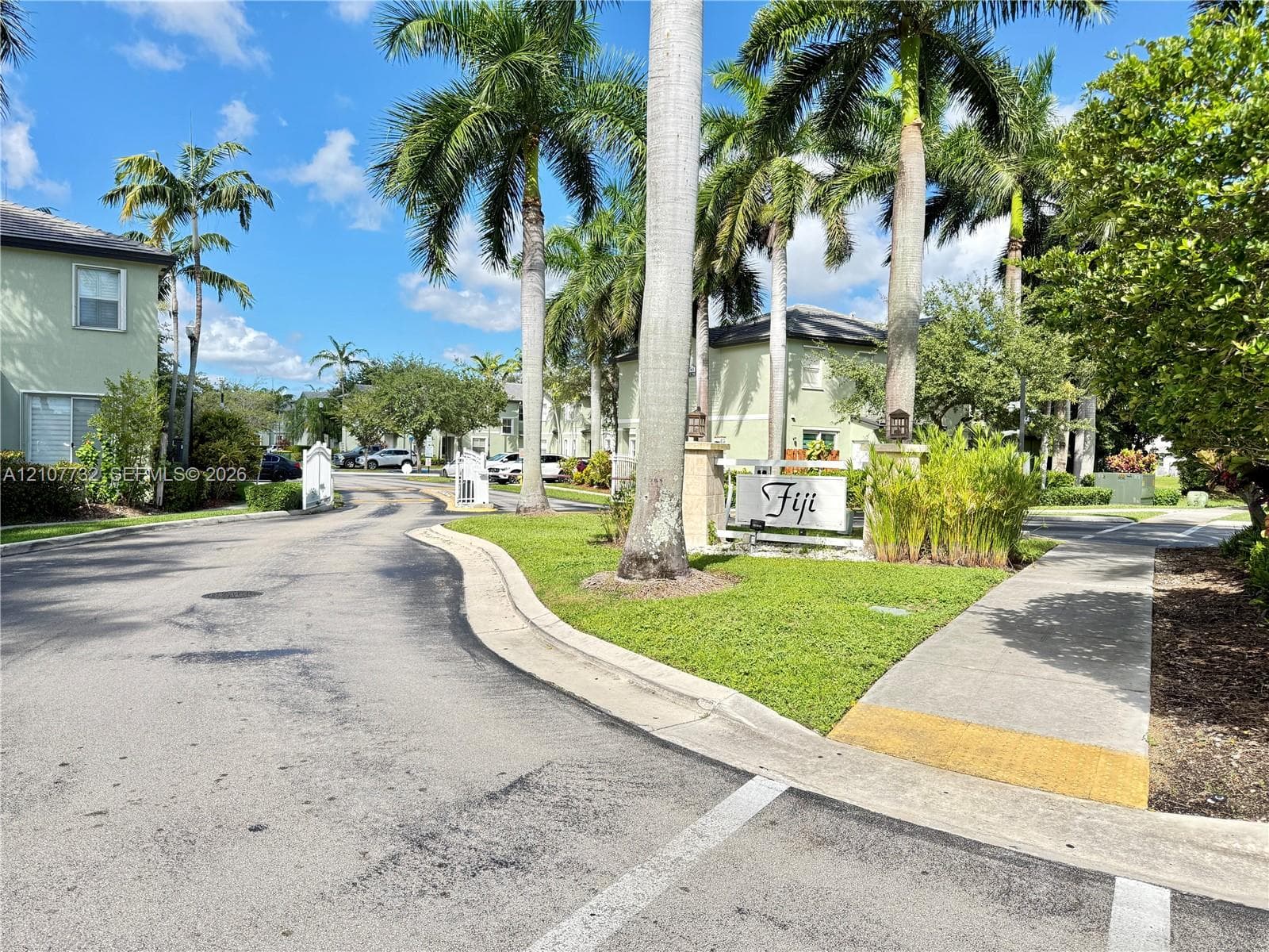 Community entrance featuring paved roadways, concrete sidewalks, established palm trees, and manicured lawn areas