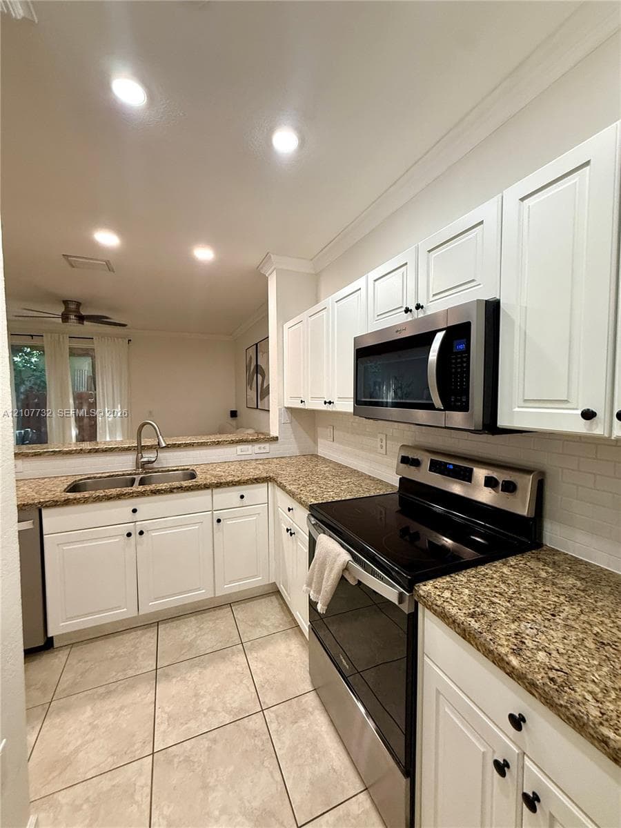 Kitchen featuring white shaker-style cabinetry, stone-finish countertops, stainless steel appliances, a tile backsplash, and ceramic tile flooring