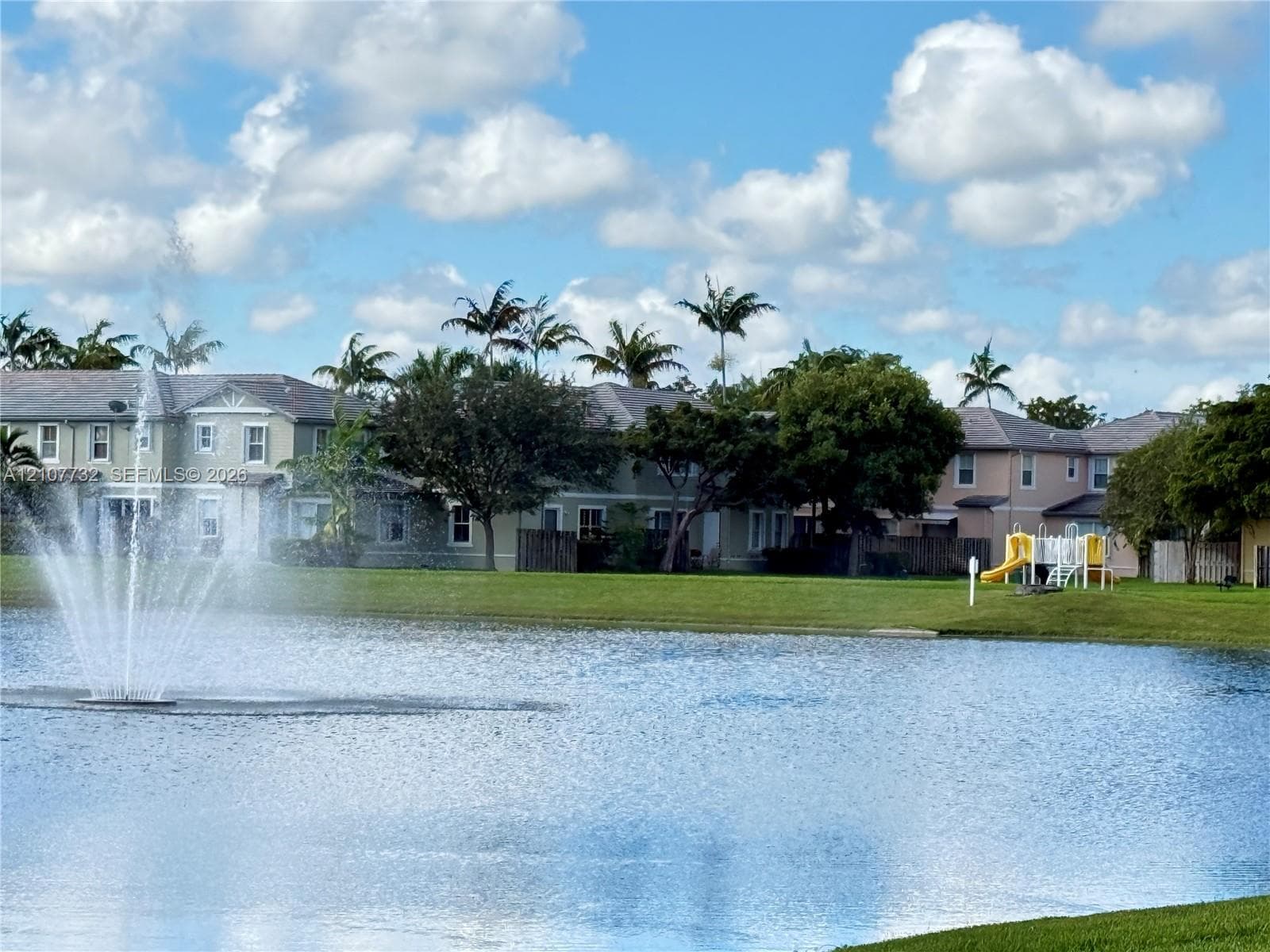 Waterfront community featuring a central fountain, manicured lawn, and mature palm trees