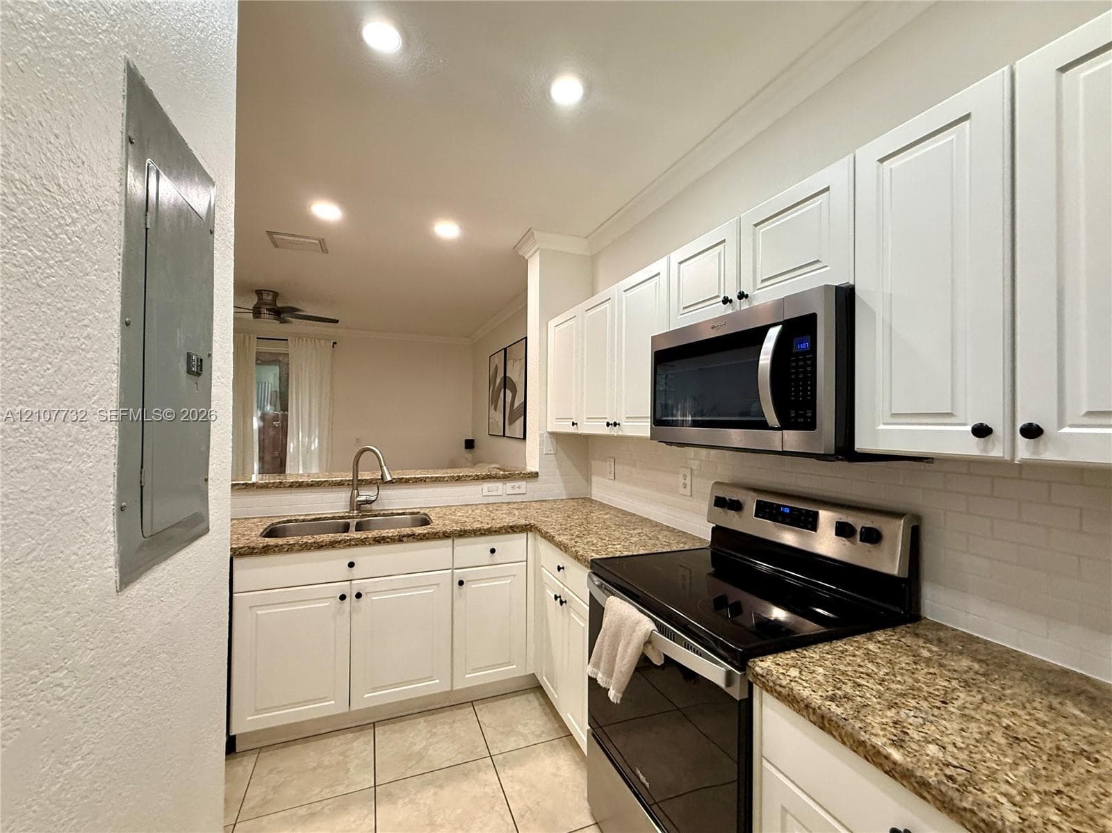 Kitchen featuring white shaker-style cabinetry, speckled stone-finish countertops, subway tile backsplash, stainless steel microwave, and dual-basin stainless steel sink