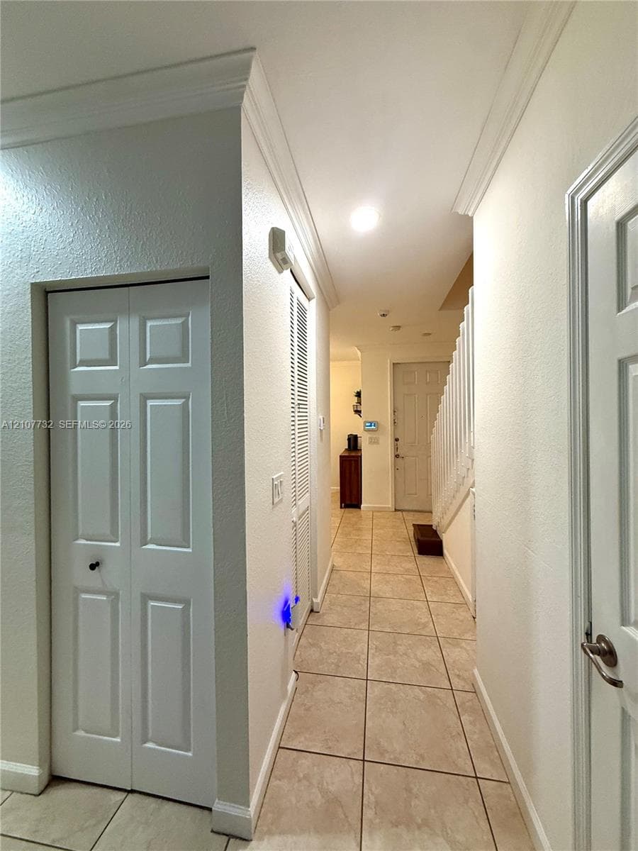 Neutral tile flooring, crown molding, paneled interior doors, and white-finish cabinetry