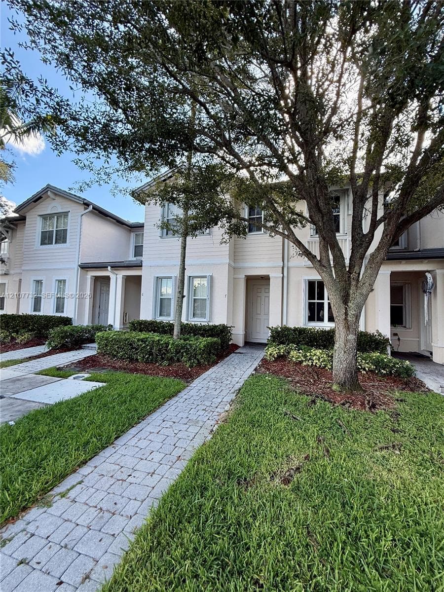 Two-story exterior featuring lap siding, paver walkways, manicured landscaping, and mature canopy trees