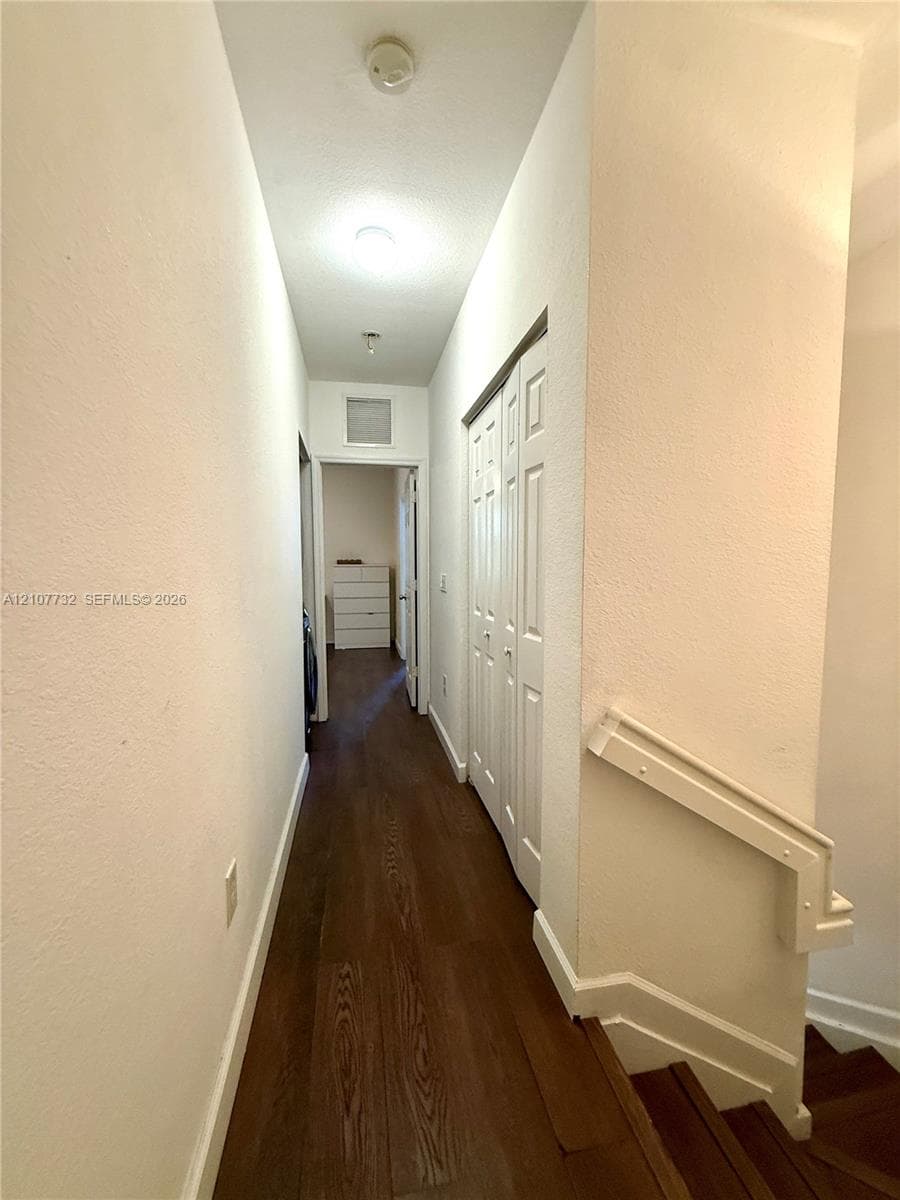 Hallway featuring wood-finish flooring, white paneled bi-fold closet doors, and a staircase with a white handrail