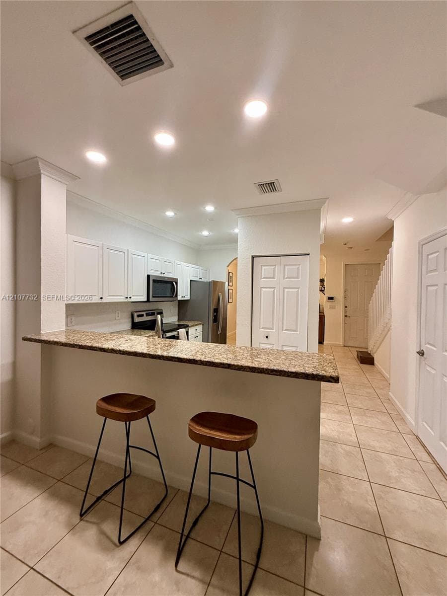 Kitchen featuring a stone-look countertop breakfast bar, white cabinetry, recessed lighting, and tile flooring
