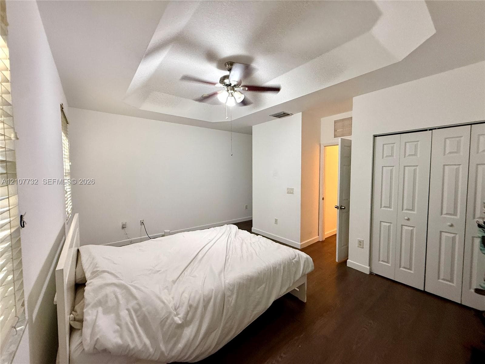 Tray ceiling featuring a central light fixture and fan, wood-finish flooring, and multi-panel bi-fold closet doors