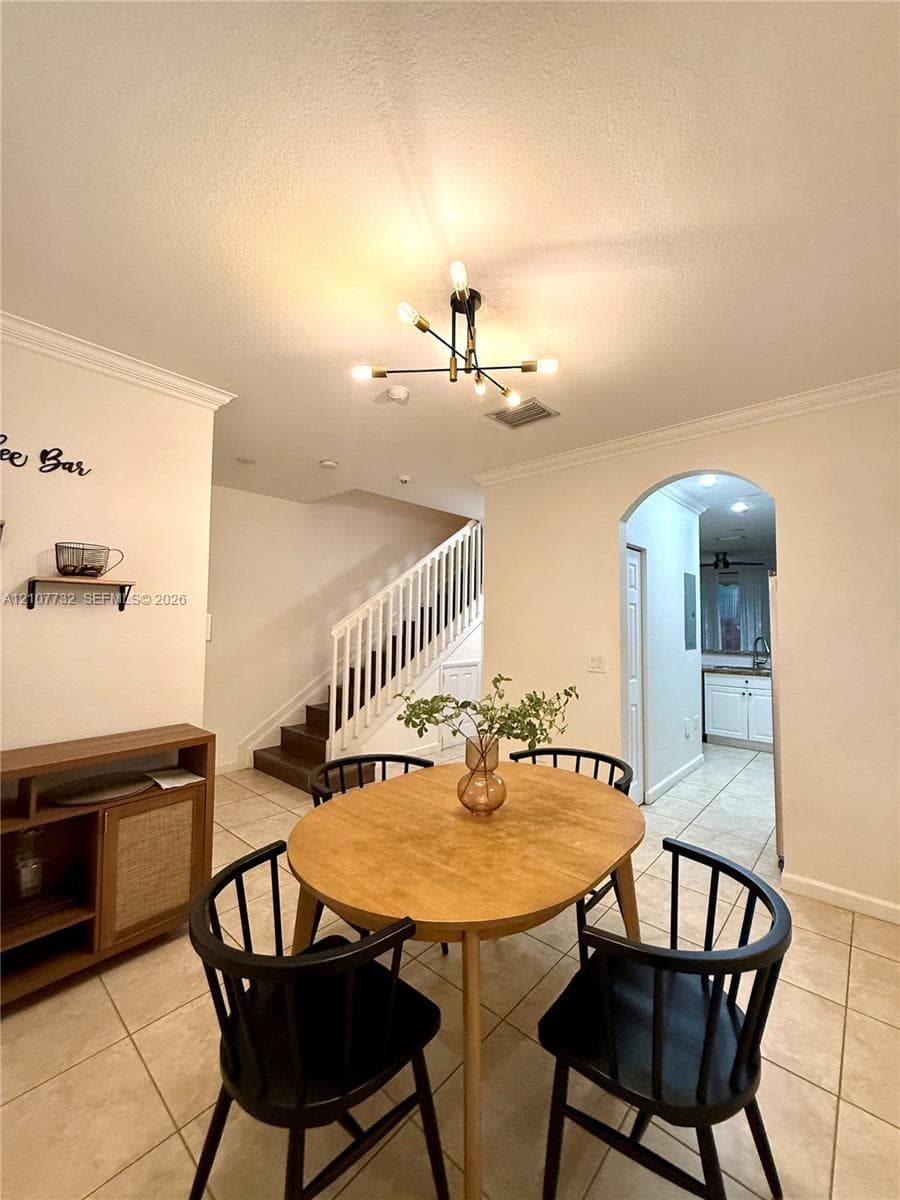 Tile flooring, crown molding, multi-arm chandelier, and arched doorway