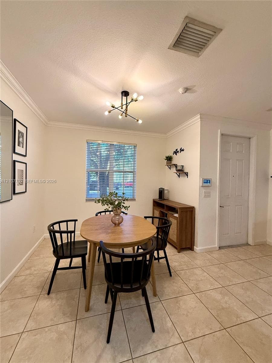 Neutral-toned interior featuring ceramic tile flooring, crown molding, multi-arm geometric ceiling lighting, and a window with horizontal blinds