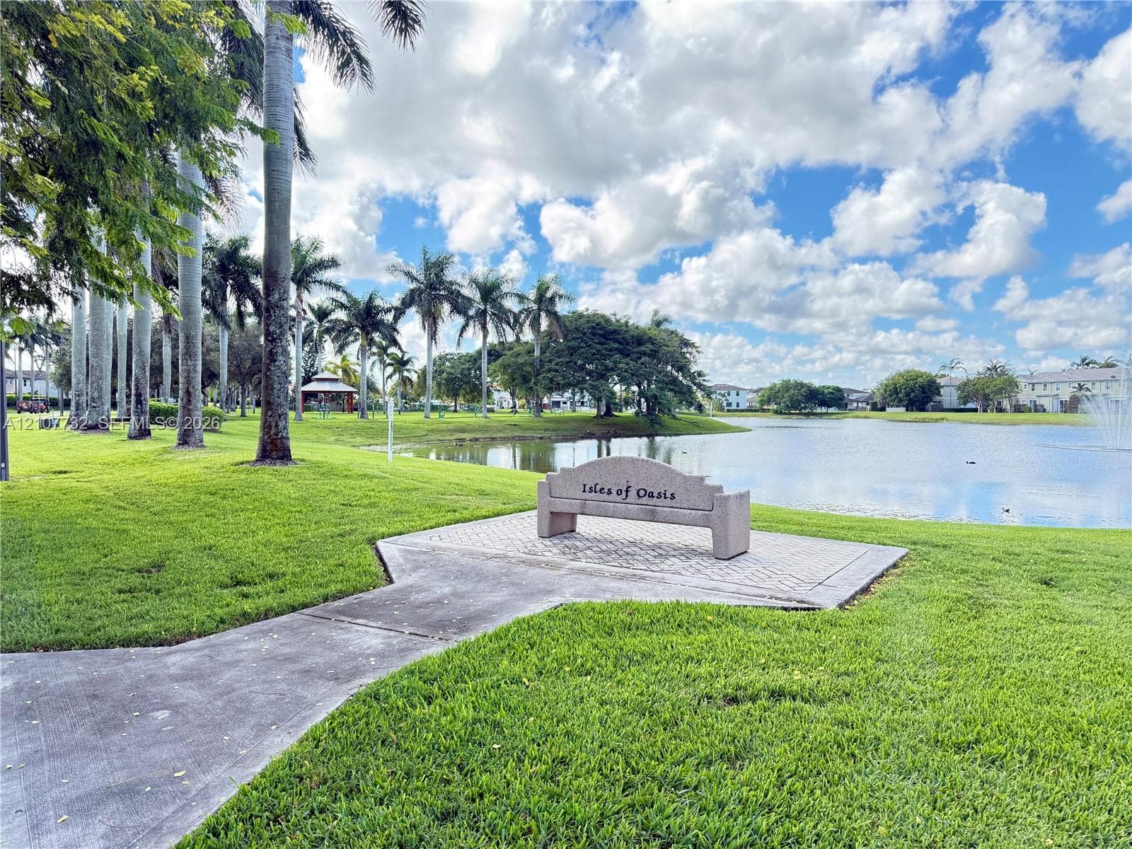 Waterfront common area featuring a paved pedestrian walkway, stone-finish bench, and mature palm trees