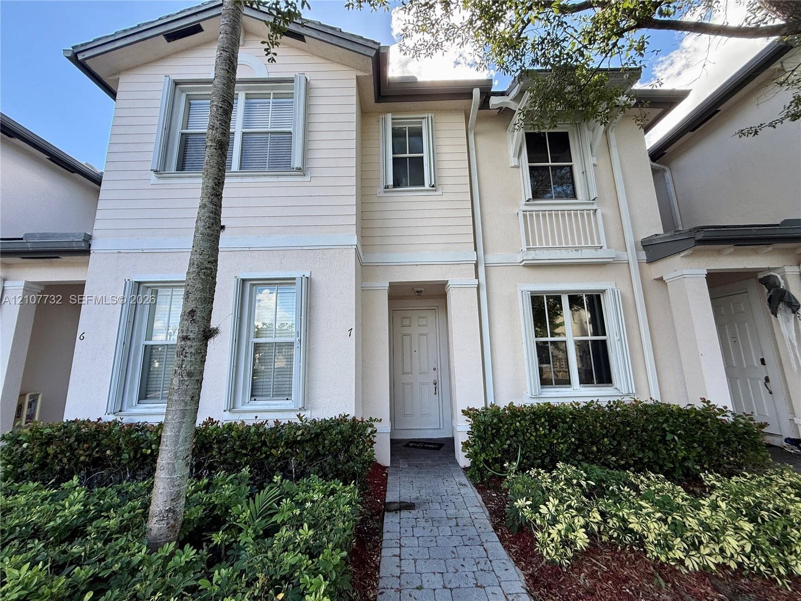 Two-story exterior featuring a mix of horizontal lap siding and textured stucco finish, a covered entryway, decorative upper-level balcony railing, and a stone-paver walkway