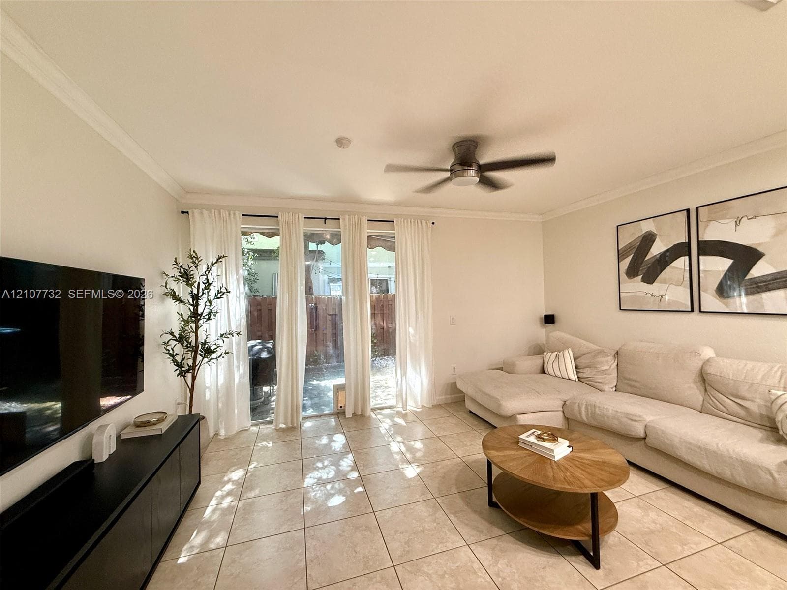 Neutral-toned tile flooring, crown molding, ceiling fan, and glass sliding doors providing external access