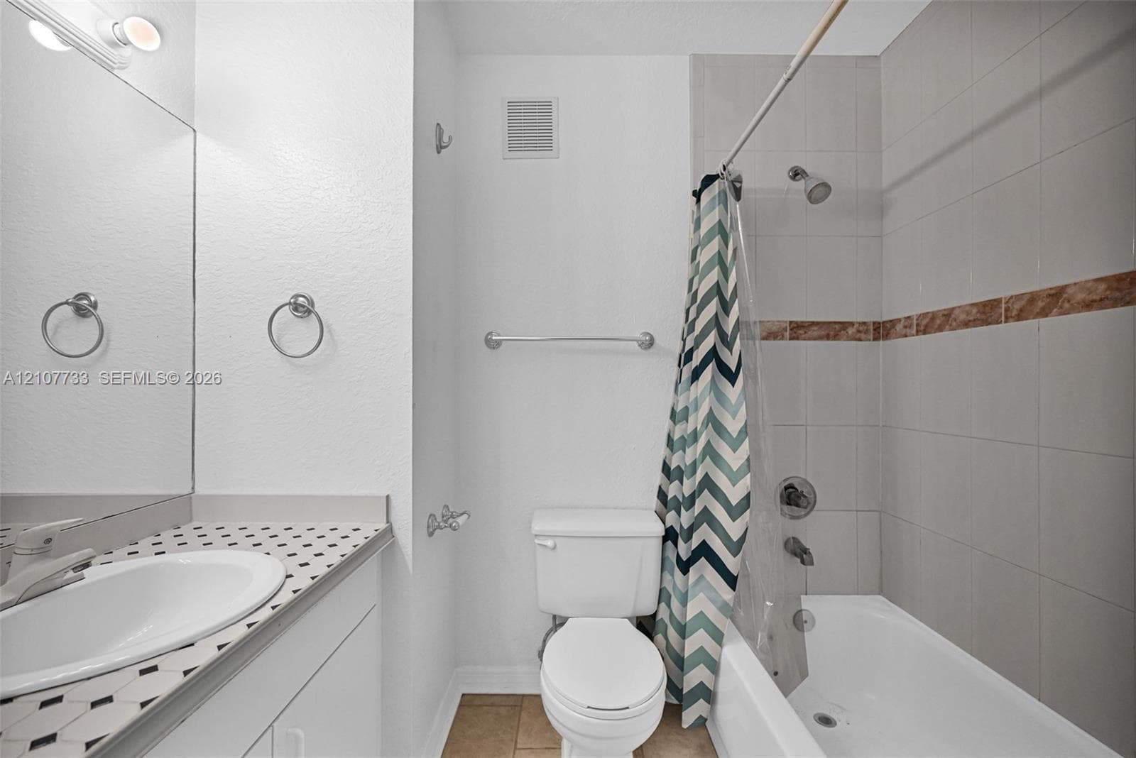 Bathroom featuring a vanity with a patterned countertop, integrated basin, wall-to-wall mirror, and a tiled shower-tub combination with a decorative accent border