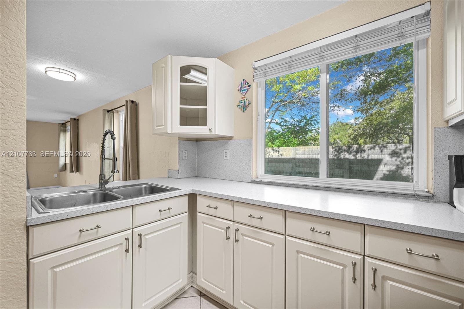 Kitchen featuring white cabinetry, solid-surface countertops, dual-basin stainless steel sink with pull-down faucet, and a large window