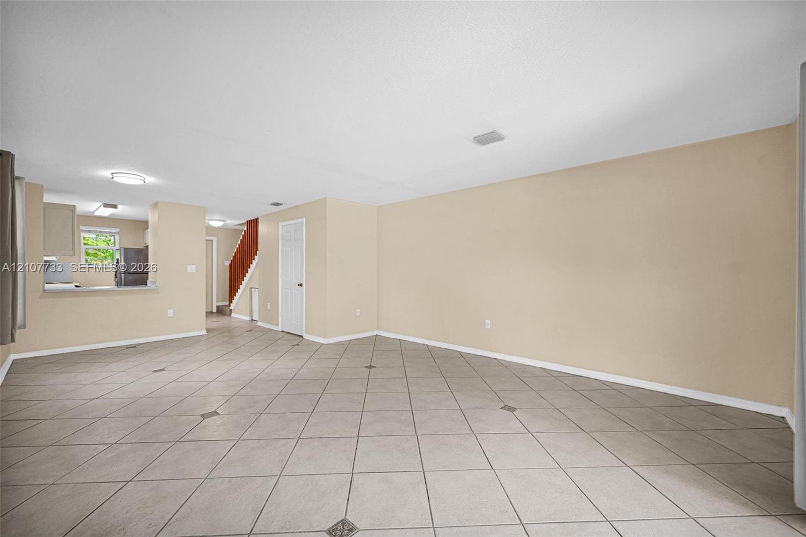 Open-concept interior featuring large-format diagonal tile flooring with decorative inlay accents, neutral wall tones, recessed ceiling lighting, and a built-in staircase with a wood-finish handrail
