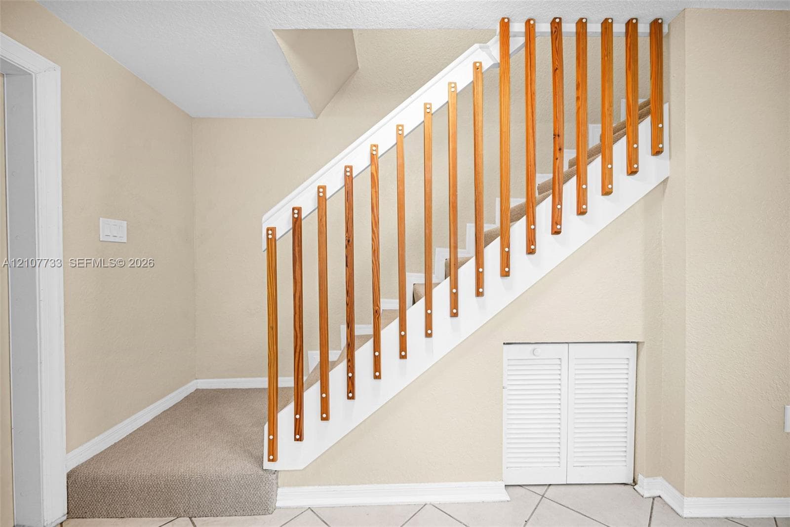 Staircase featuring white painted stringers, natural wood vertical balusters, carpeted treads, and built-in louvered storage cabinetry