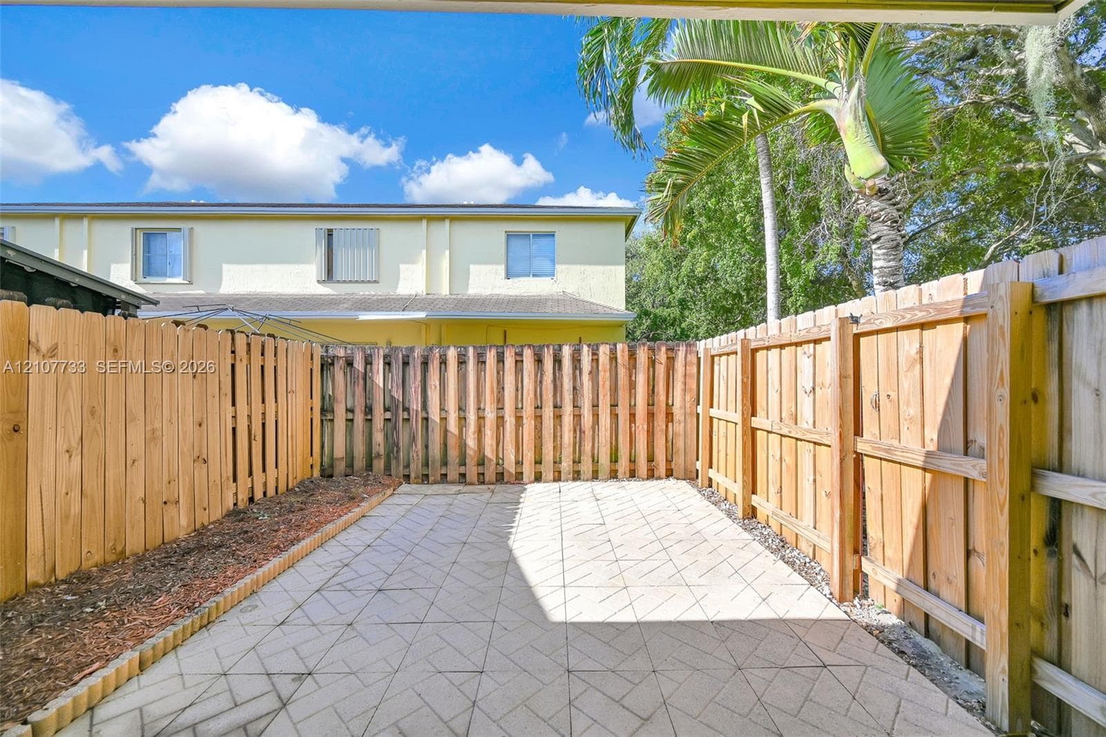 Private patio featuring patterned concrete pavers and enclosed by a wood-slat privacy fence