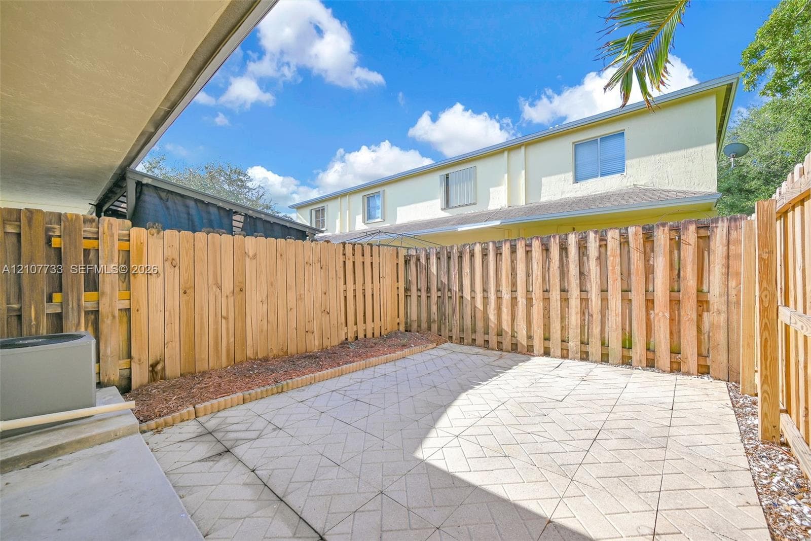 Private patio area featuring stone-paver flooring, enclosed by full-height wood fencing