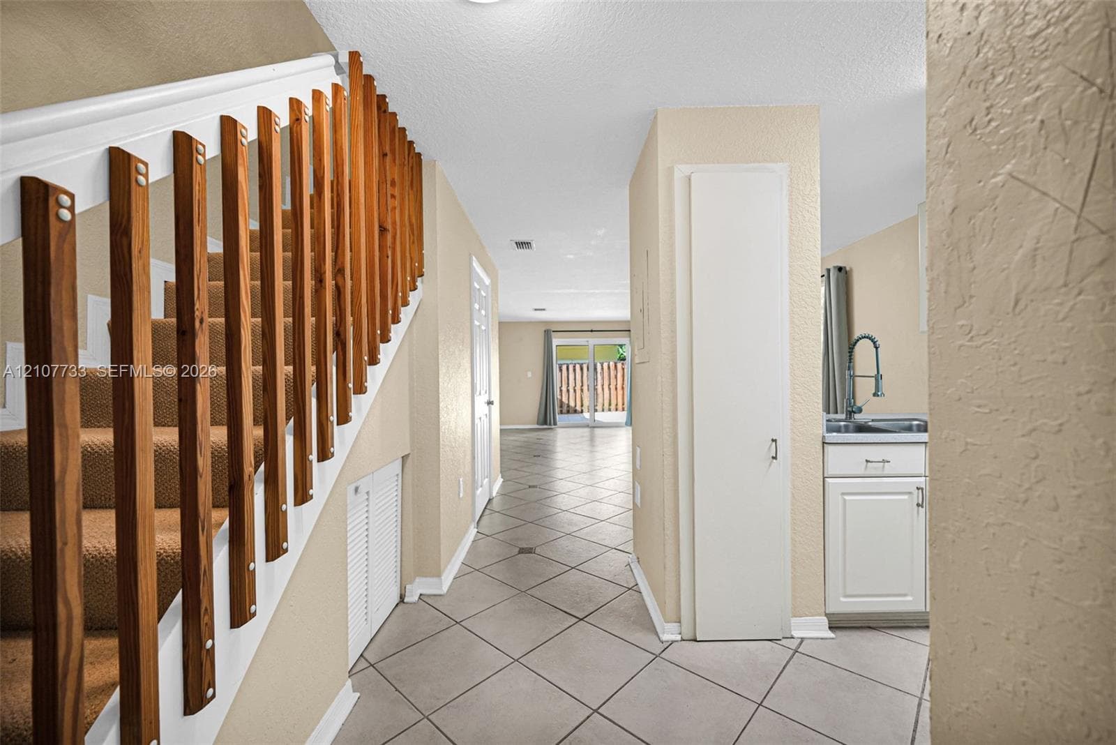 Interior area featuring ceramic tile flooring, staircase with vertical wood balusters, built-in floor-to-ceiling cabinetry, and a kitchenette area with a stainless steel sink and white cabinetry