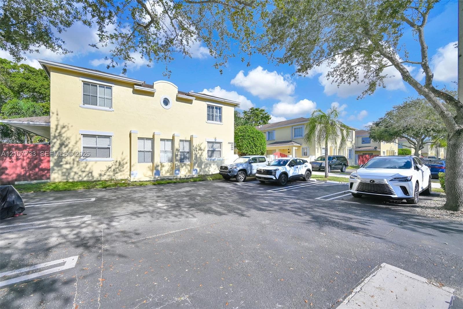 Two-story stucco exterior featuring a circular accent window, multi-paned windows, pilasters, and dedicated asphalt parking area