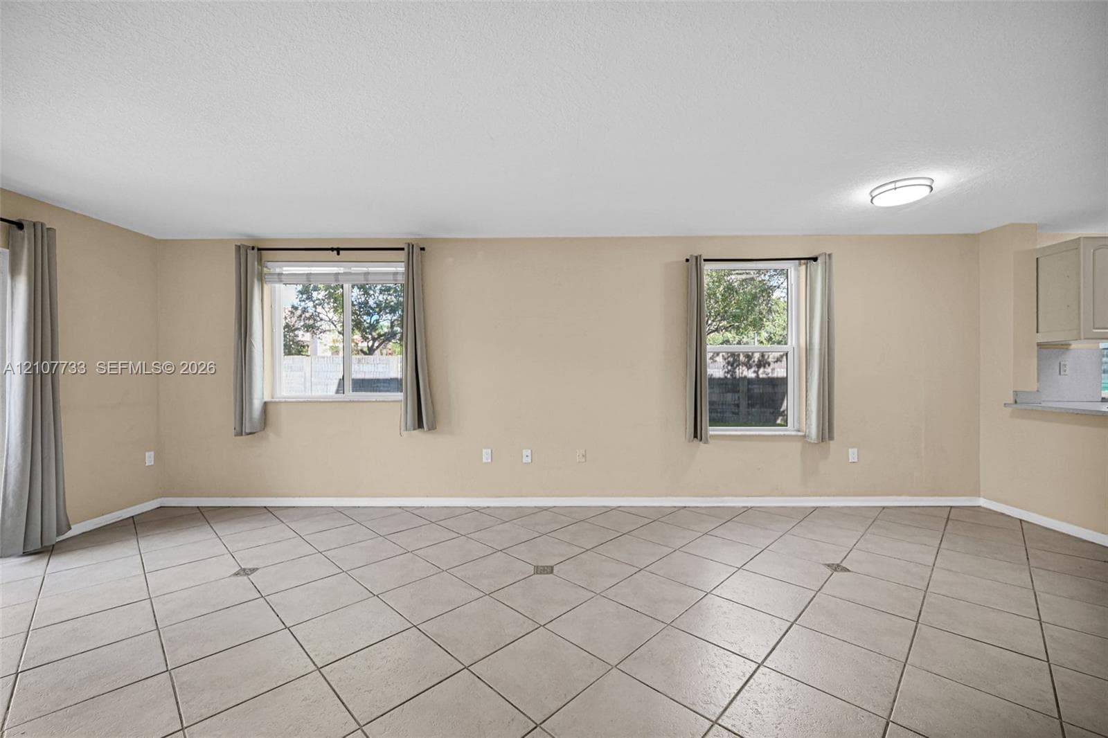 Spacious room featuring neutral wall tones, large-format tile flooring, dual windows, and recessed ceiling lighting