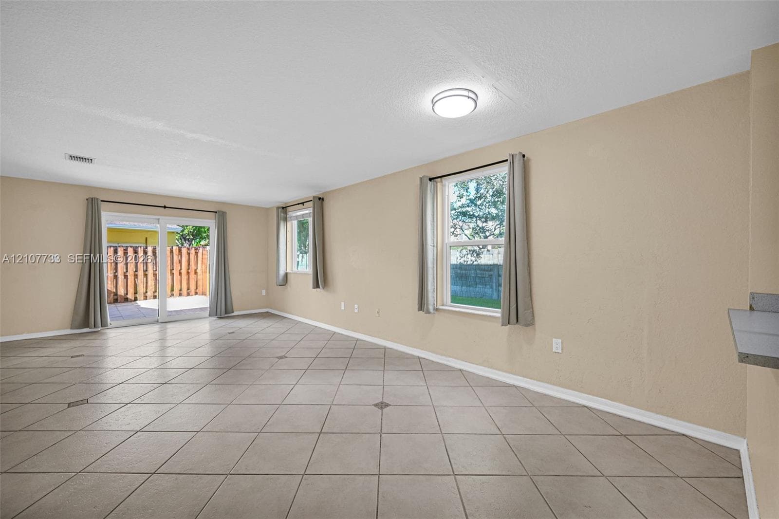 Open-concept interior featuring neutral wall tones, large-format tile flooring, dual-pane windows, and sliding glass doors with exterior access