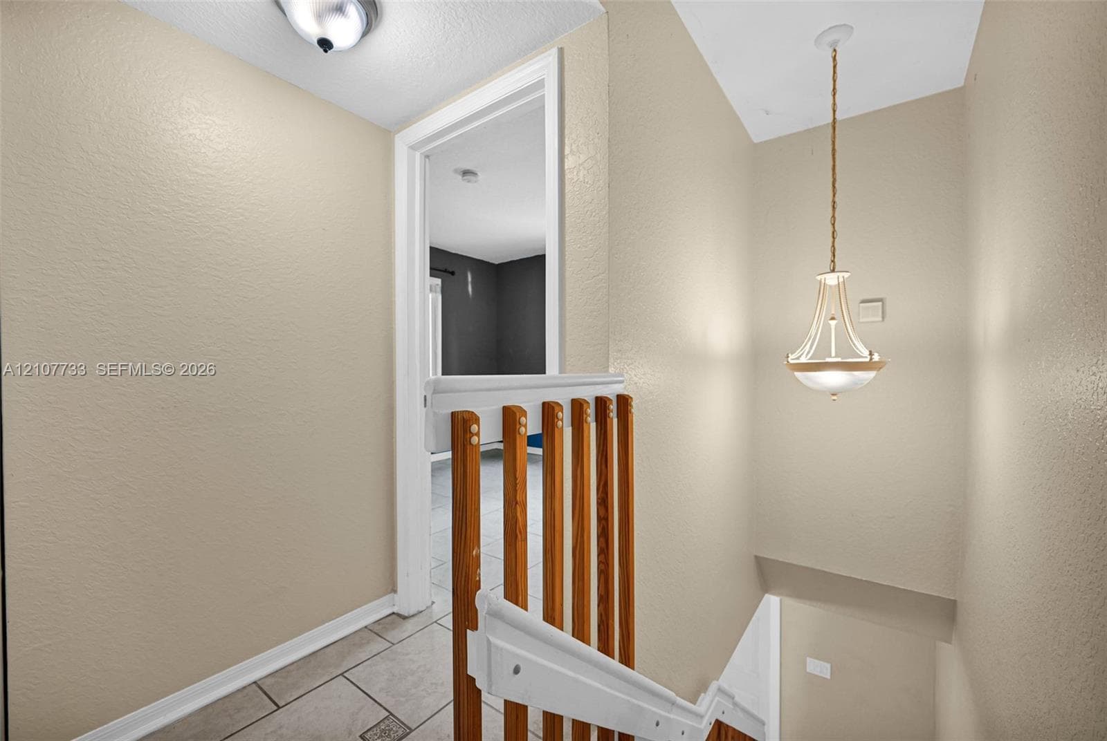 Staircase featuring wood-slat railings, a decorative metal pendant light fixture, ceiling-mounted dome lighting, and neutral tile flooring