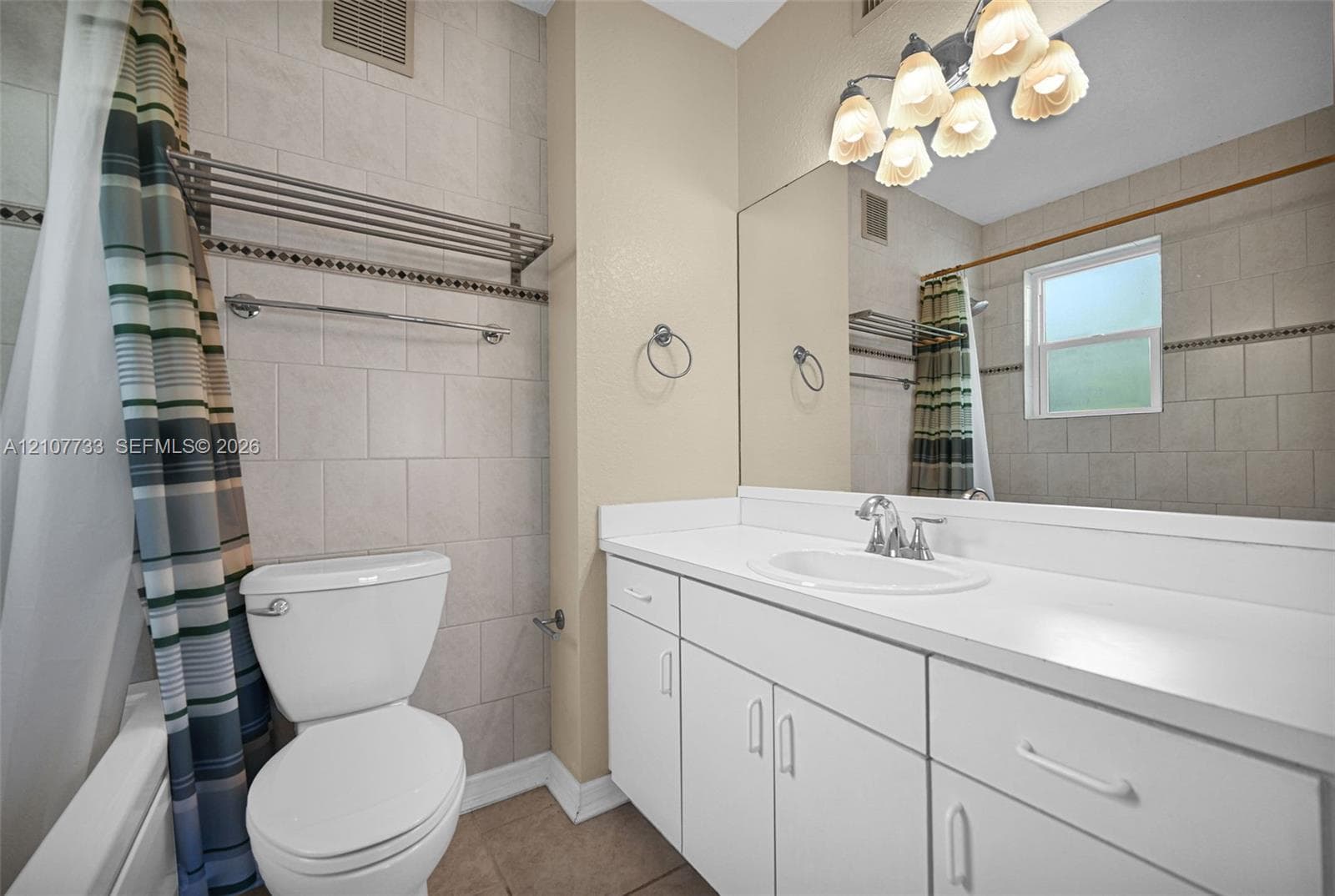Bathroom featuring a vanity with a white countertop and oval under-mount sink, full-width wall mirror, five-light fixture, and tile-surround tub area with decorative accent inlay
