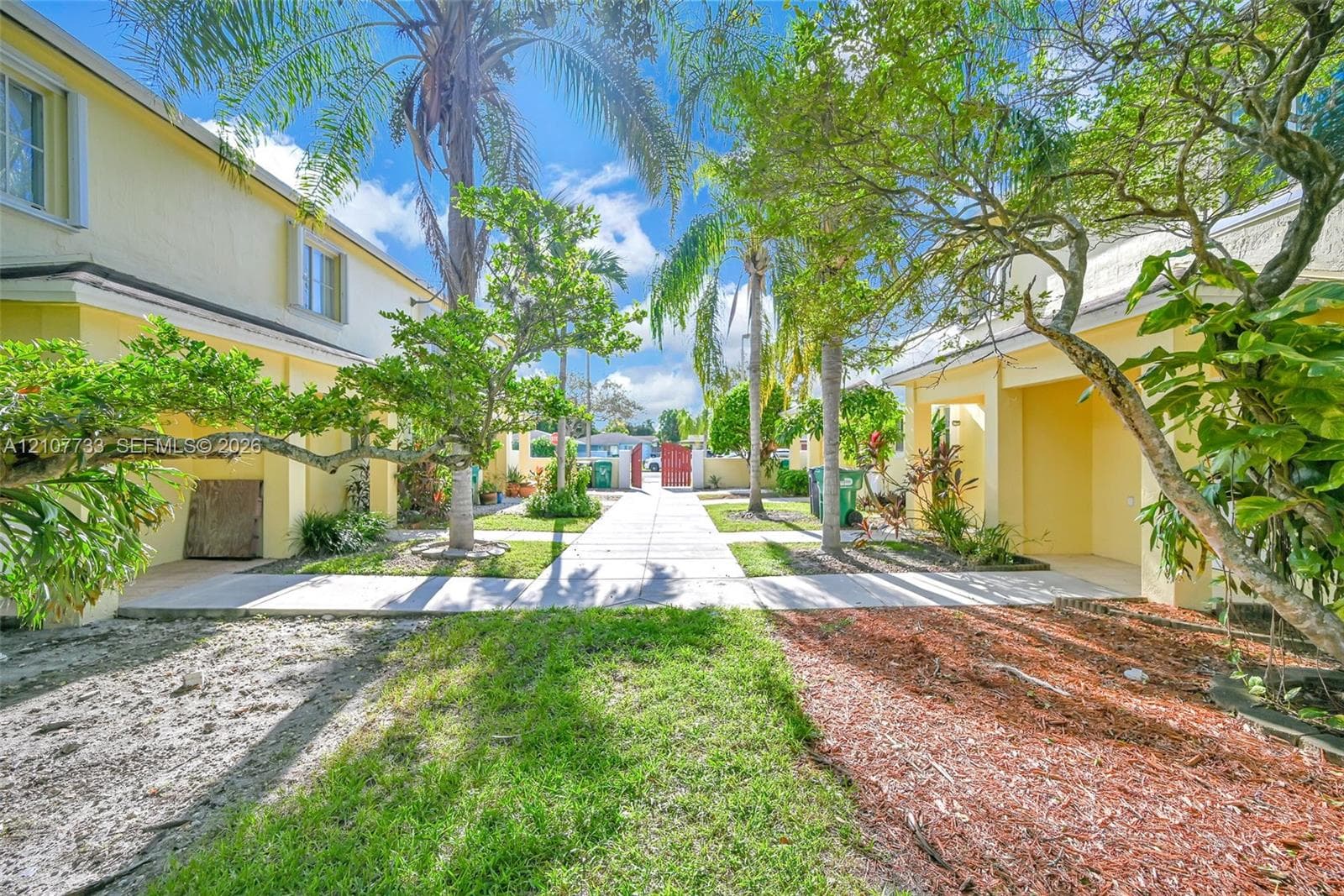 Exterior courtyard featuring paved walkways, mature palm trees, stucco building siding, and metal gated access
