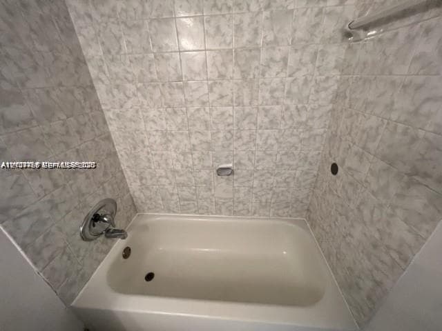 Bathtub enclosure featuring full-height ceramic wall tiling, polished chrome faucet, and integrated metal shower rod