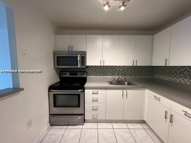 Kitchen featuring white cabinetry, stainless steel microwave and range, solid-surface countertops, mosaic tile backsplash, and light-toned tile flooring