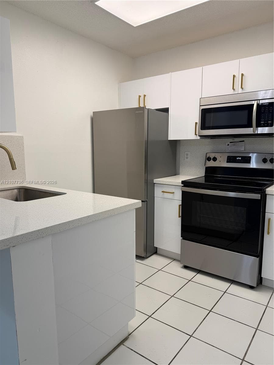 Kitchen featuring white cabinetry with gold-tone hardware, stone-finish countertops, stainless steel appliances, and ceramic tile flooring