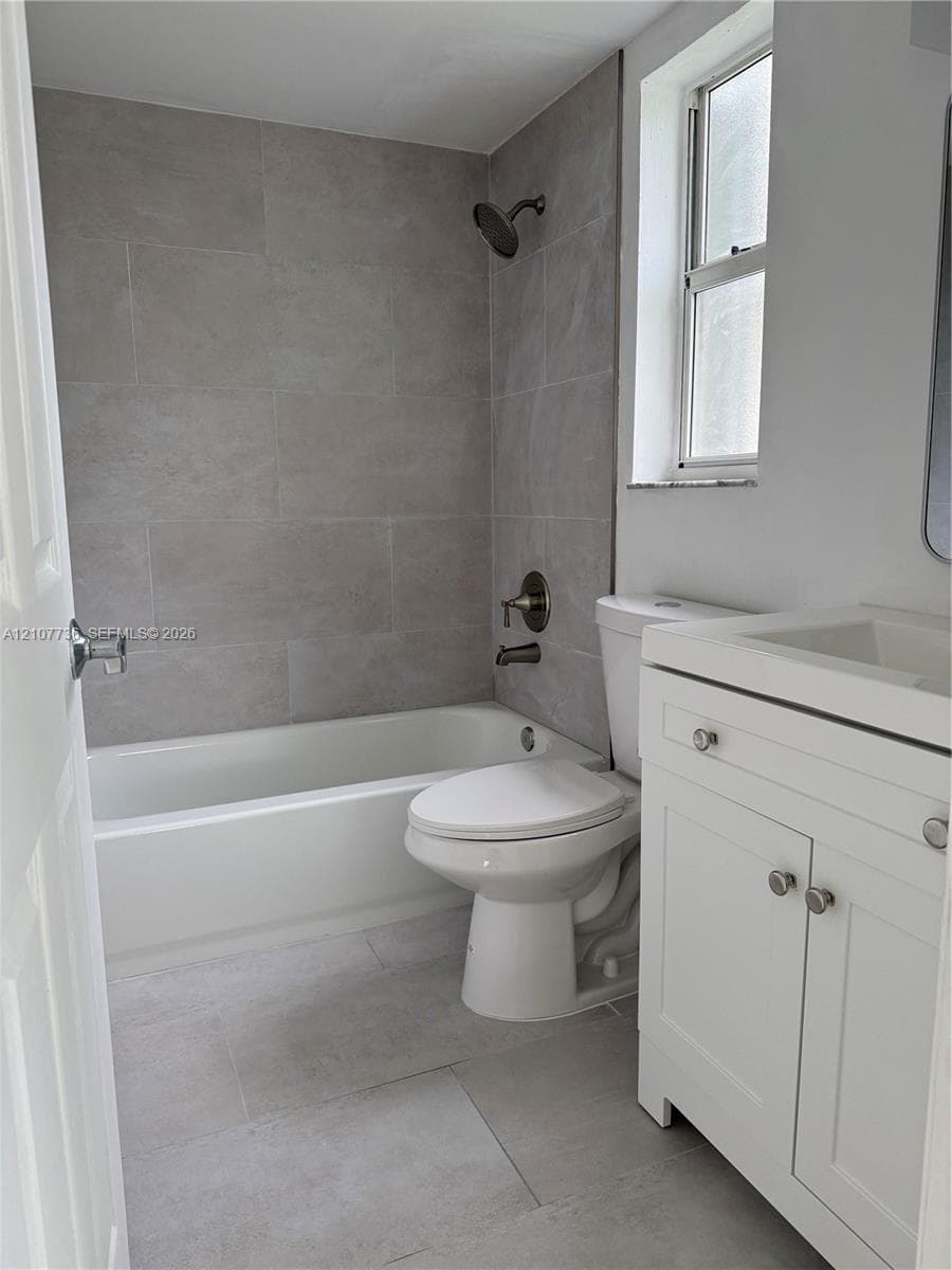 Bathroom featuring a white vanity cabinet with a integrated sink, gray tile surround for the tub, large-format floor tiling, and bronze-tone shower fixtures
