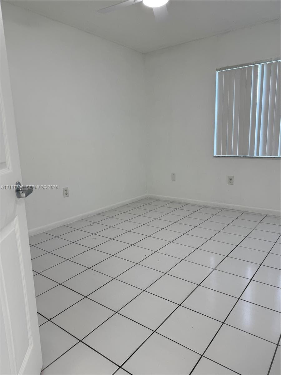 Neutral-toned room featuring ceramic tile flooring, vertical window blinds, and a ceiling fan with integrated lighting
