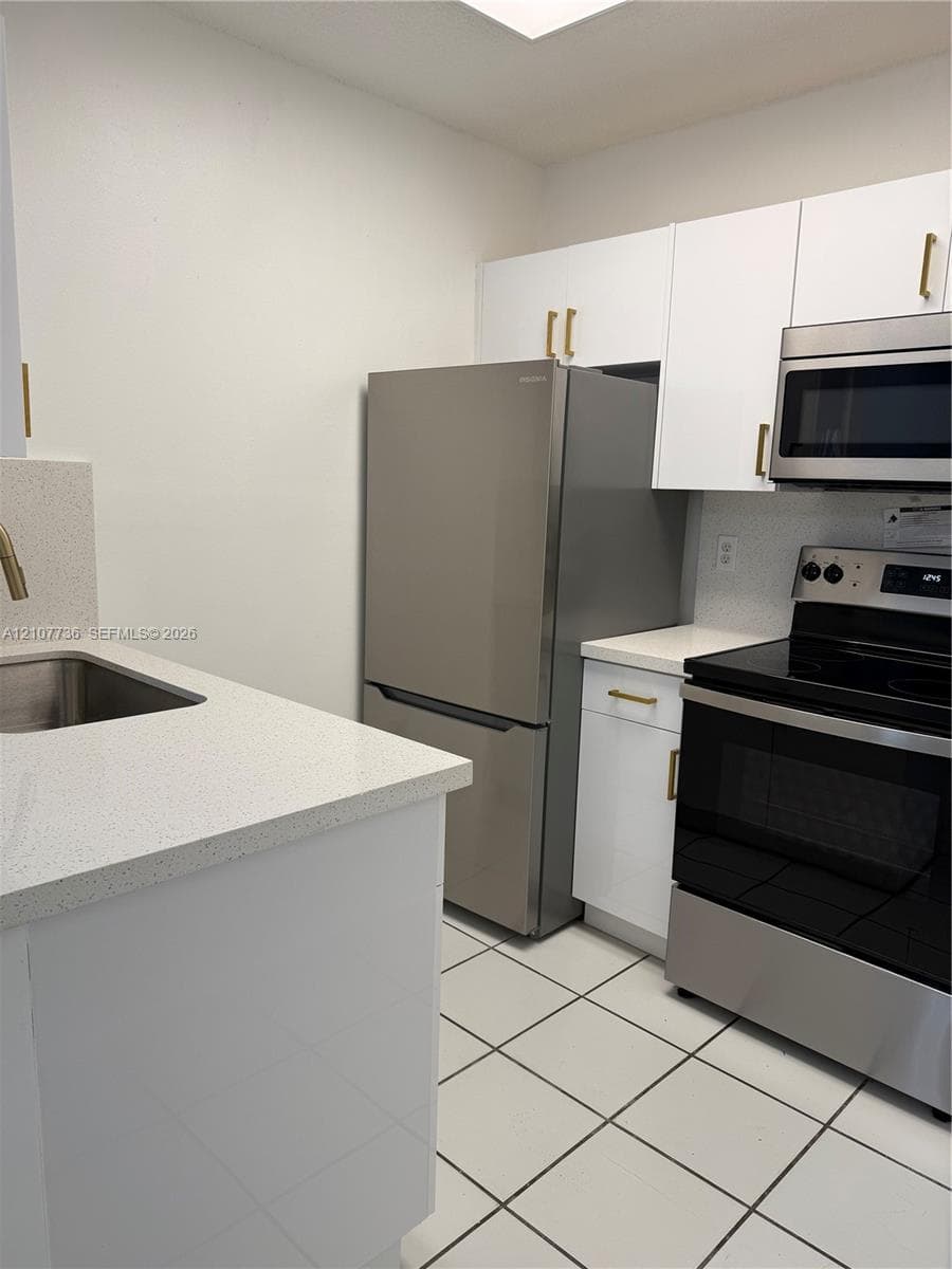Kitchen featuring white cabinetry with metallic pulls, stone-composite countertops, stainless steel appliances, and tile flooring