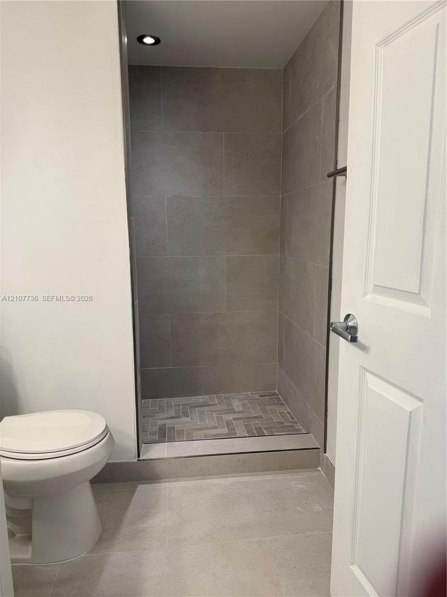 Shower featuring large-format neutral wall tile, herringbone-patterned floor tile, recessed lighting, and a white two-panel door