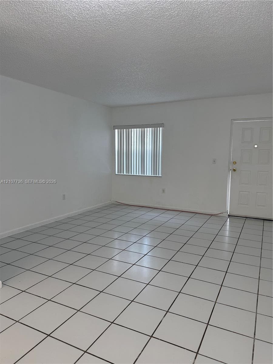 Neutral interior space featuring white walls, square ceramic tile flooring, and vertical window blinds