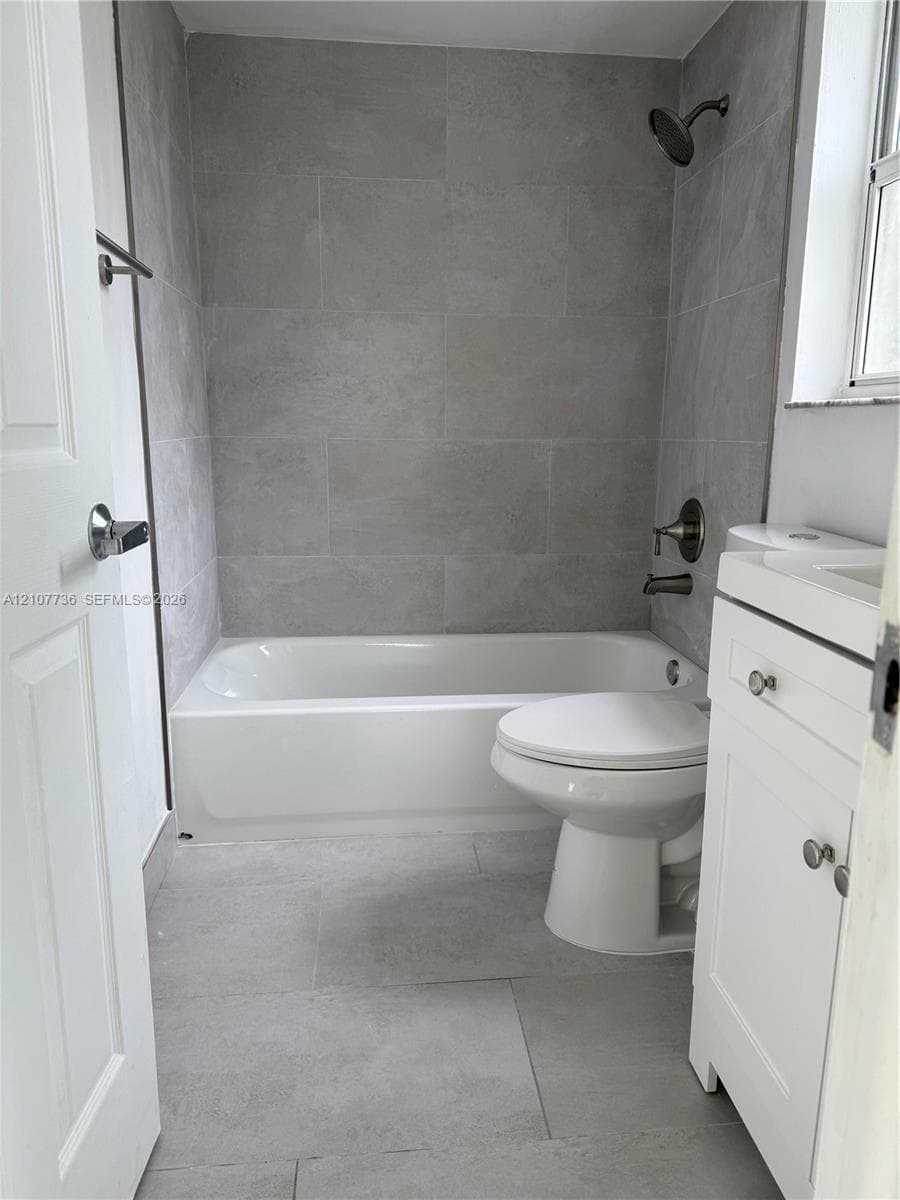 Bathroom featuring large-format gray tile flooring and wall surround, a white vanity with integrated basin, and brushed-finish fixtures