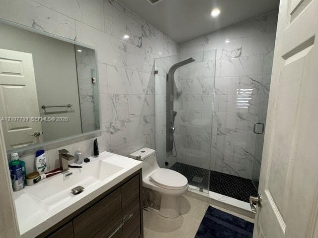 Bathroom featuring a wood-finish vanity with an integrated basin, frameless glass walk-in shower with a rainfall shower panel, wall-to-wall large-format tile, and a backlit mirror