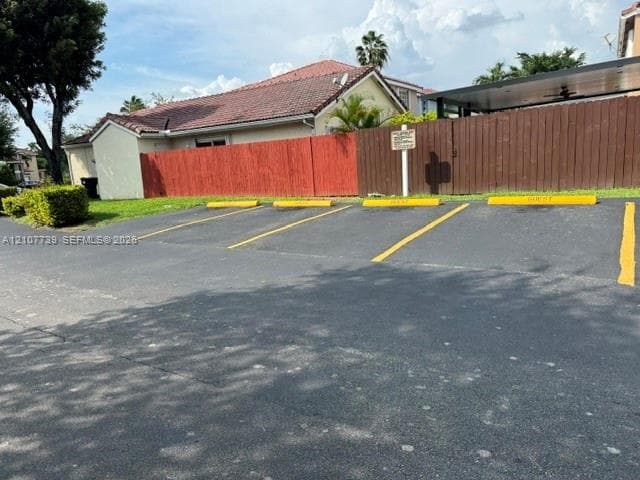 Asphalt surface parking area with four designated stalls, painted yellow wheel stops, and a tall wood perimeter fence