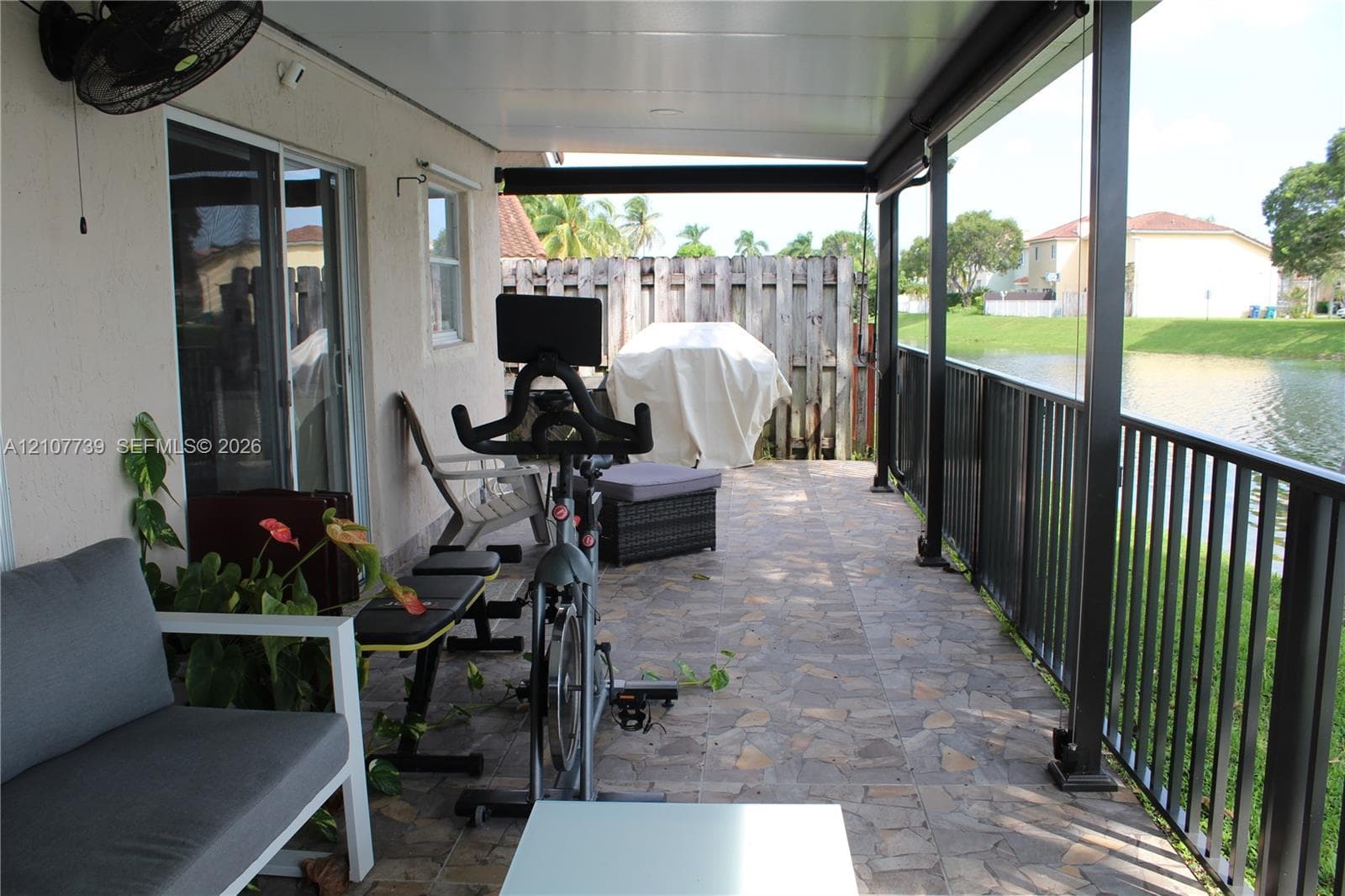 Covered patio featuring stone-tiled flooring, a ceiling-mounted fan, and a metal perimeter railing overlooking a water feature