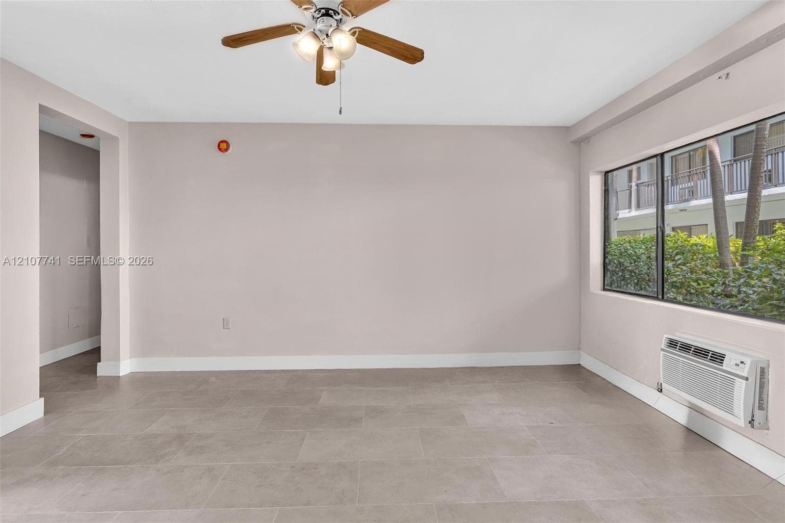 Interior space featuring large-format tile flooring, neutral wall paint, a central ceiling fan with integrated lighting, a single-pane window, and a decorative partition wall