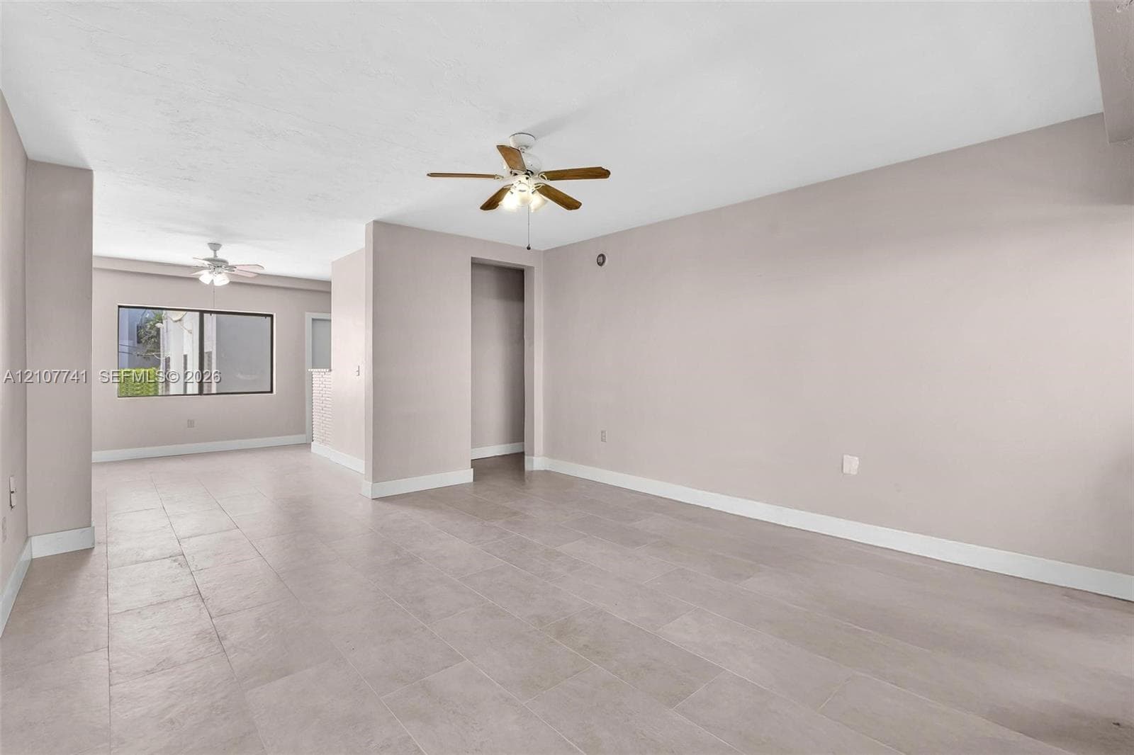 Neutral-toned interior space featuring light-colored tile flooring, smooth wall finishes, and multiple ceiling fans with integrated lighting fixtures