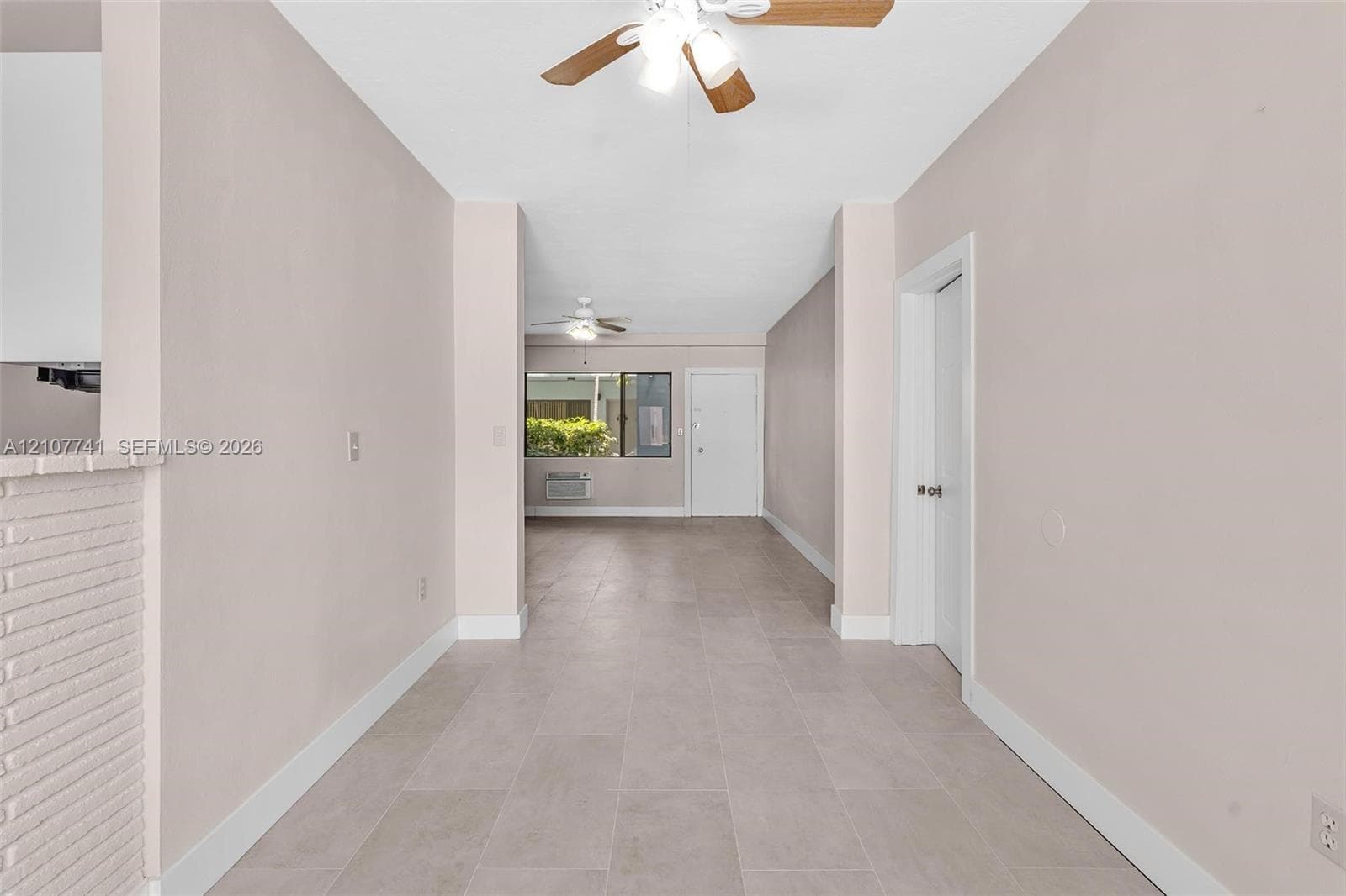 Neutral-toned interior featuring large-format ceramic tile flooring, a built-in reach-in closet with integrated shelving, and a ceiling-mounted light fixture with a five-blade fan
