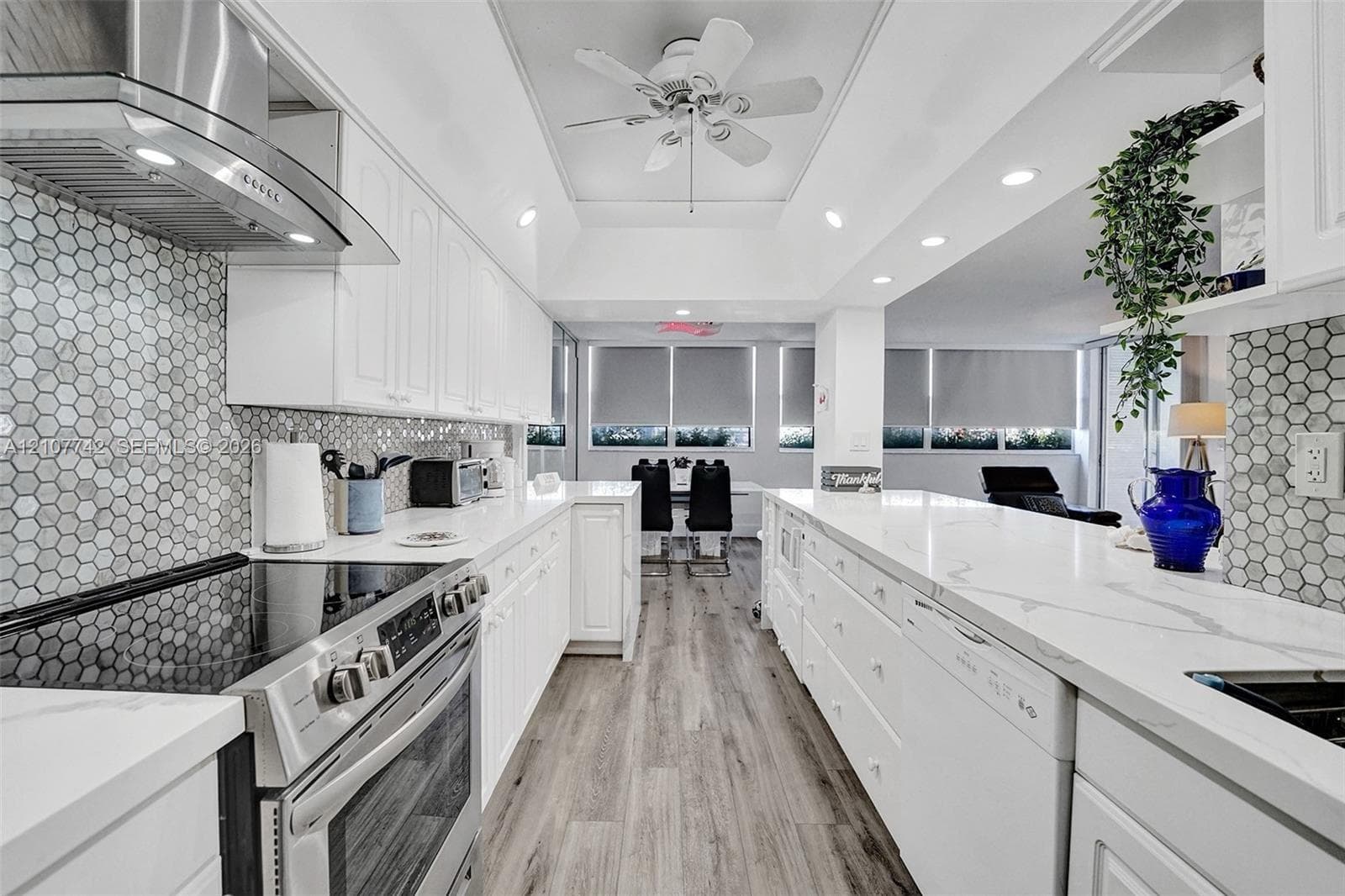 Kitchen featuring white cabinetry, stone-finish countertops, hexagonal tile backsplash, stainless steel range with overhead ventilation, and wood-finish flooring