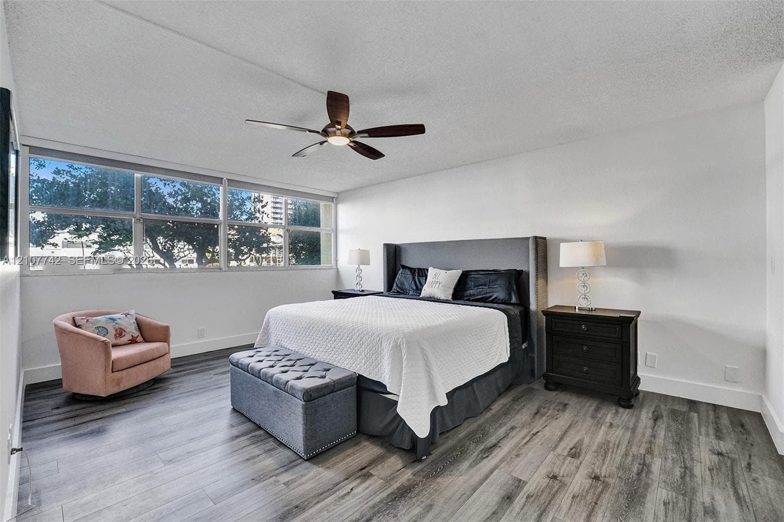 Wood-finish flooring, expansive window pane configuration, and a centrally mounted ceiling fan with integrated lighting