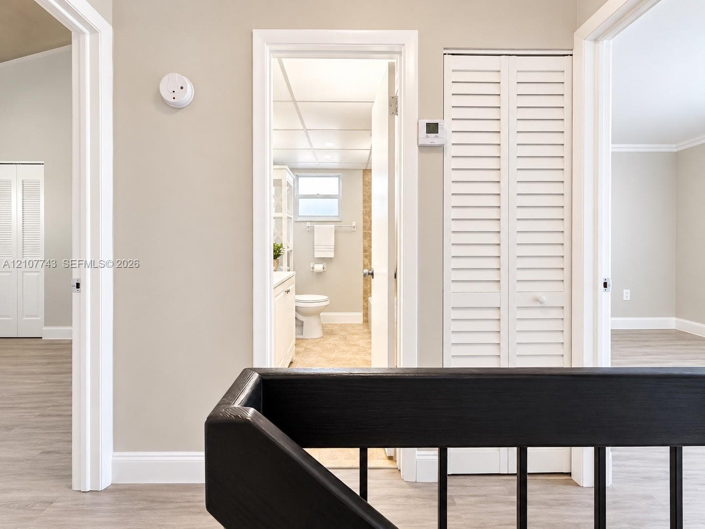 Hallway featuring wood-finish flooring, white louvered-door closets, and a black metal handrail