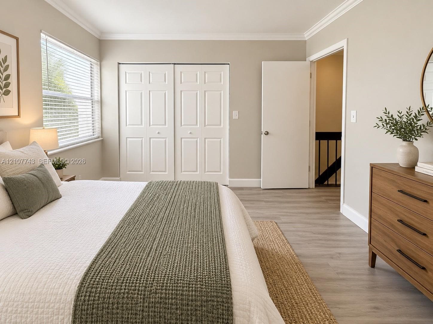 Room featuring wood-finish flooring, crown molding, dual-panel sliding closet doors, and horizontal slat blinds