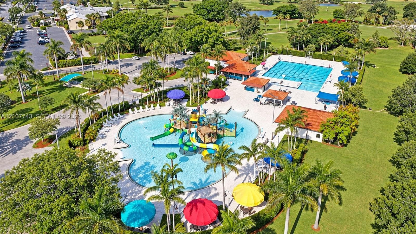 Community multi-lane lap pool, a water play area with slides, terra-cotta tiled pool structures, and mature palm landscaping